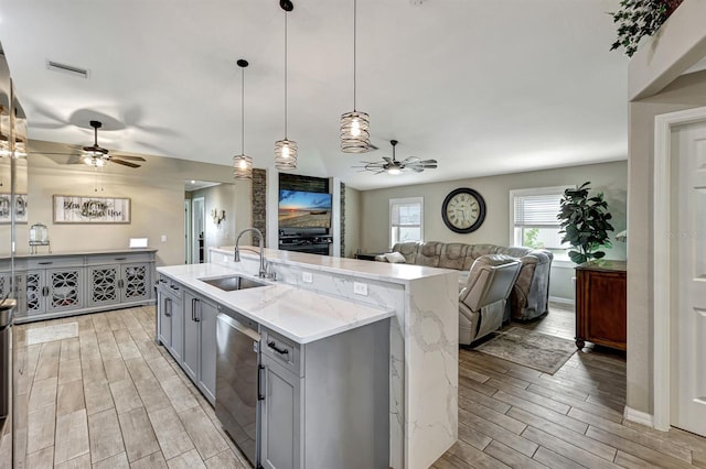 kitchen featuring dishwasher, hanging light fixtures, sink, gray cabinetry, and a kitchen island with sink