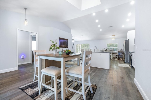 kitchen with dark wood-type flooring, decorative light fixtures, vaulted ceiling, stainless steel refrigerator, and white cabinets