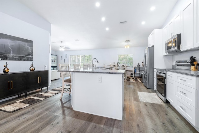 kitchen featuring white cabinetry, stainless steel appliances, a breakfast bar area, and dark stone counters