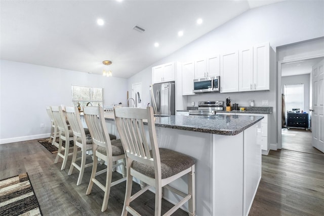 kitchen with white cabinetry, a center island with sink, dark stone counters, a kitchen breakfast bar, and stainless steel appliances