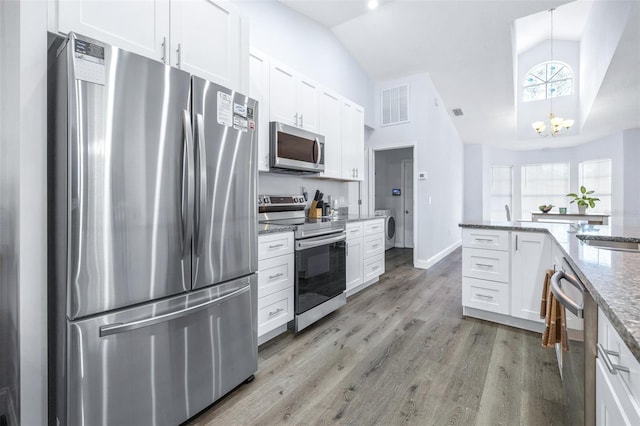 kitchen featuring appliances with stainless steel finishes, decorative light fixtures, lofted ceiling, white cabinets, and light stone countertops