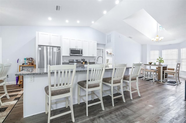 kitchen with dark wood-type flooring, a kitchen island with sink, stainless steel appliances, white cabinets, and a kitchen bar