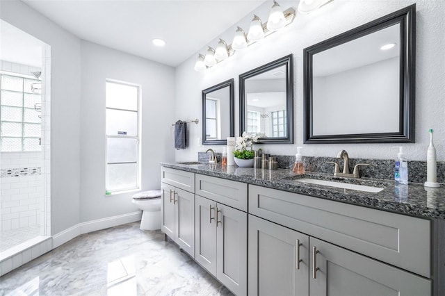 bathroom featuring tiled shower, vanity, toilet, and a wealth of natural light