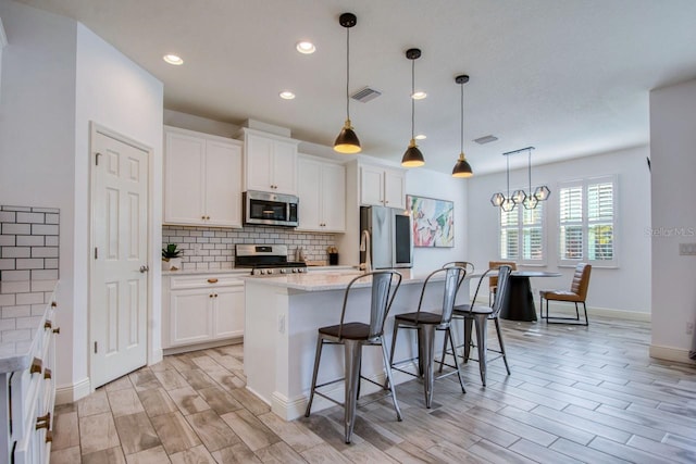 kitchen featuring decorative light fixtures, a breakfast bar area, white cabinets, stainless steel appliances, and a center island with sink