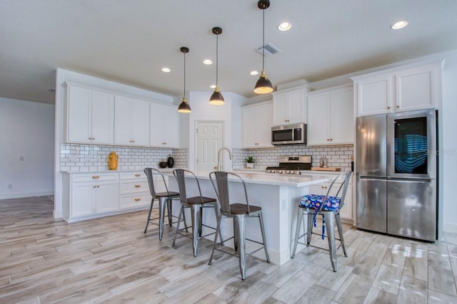 kitchen featuring white cabinetry, decorative light fixtures, stainless steel appliances, and a center island with sink