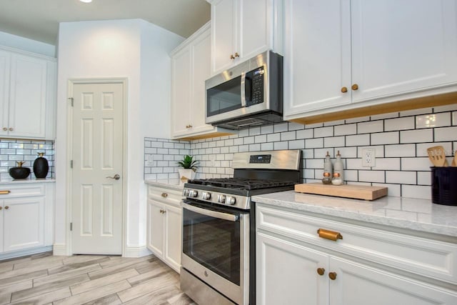 kitchen featuring light stone countertops, white cabinetry, appliances with stainless steel finishes, and decorative backsplash