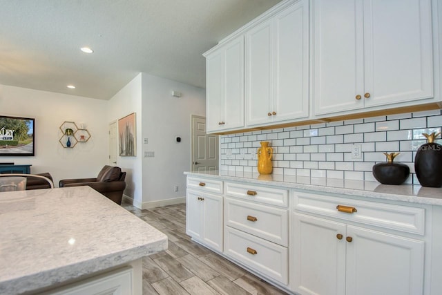 kitchen with white cabinetry, tasteful backsplash, light hardwood / wood-style floors, and light stone counters