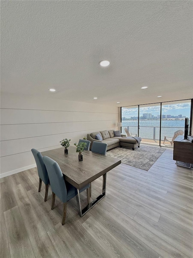 dining room featuring floor to ceiling windows, a water view, a textured ceiling, and light wood-type flooring