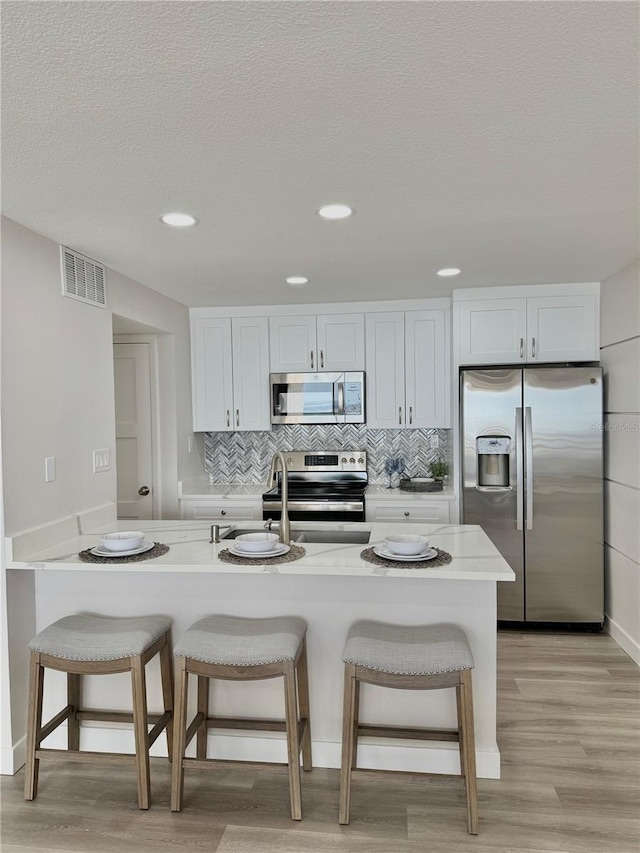 kitchen featuring appliances with stainless steel finishes, a breakfast bar, white cabinets, and light stone counters