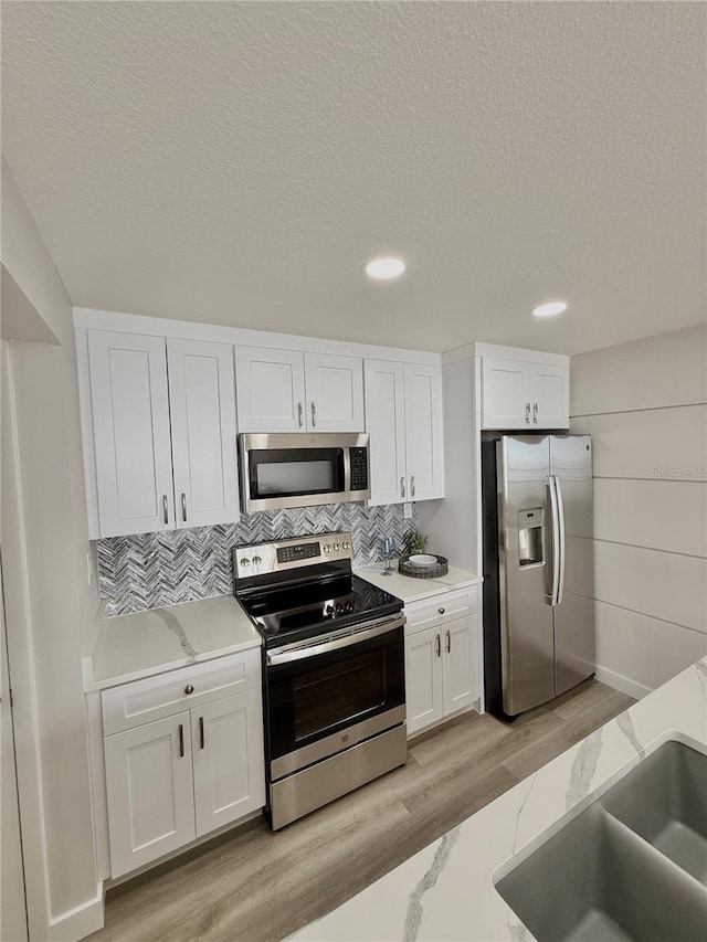 kitchen featuring stainless steel appliances, light stone countertops, light hardwood / wood-style floors, decorative backsplash, and white cabinets