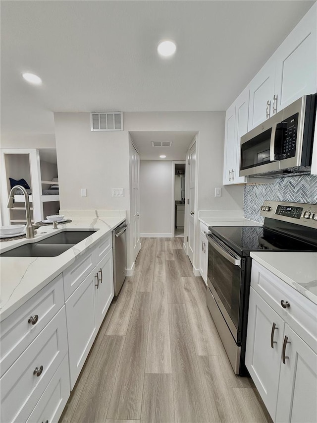 kitchen with sink, light hardwood / wood-style flooring, appliances with stainless steel finishes, white cabinetry, and light stone counters