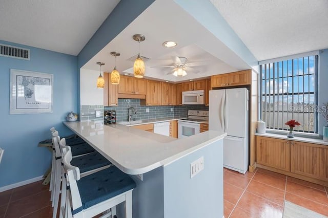 kitchen featuring pendant lighting, a breakfast bar area, decorative backsplash, kitchen peninsula, and white appliances