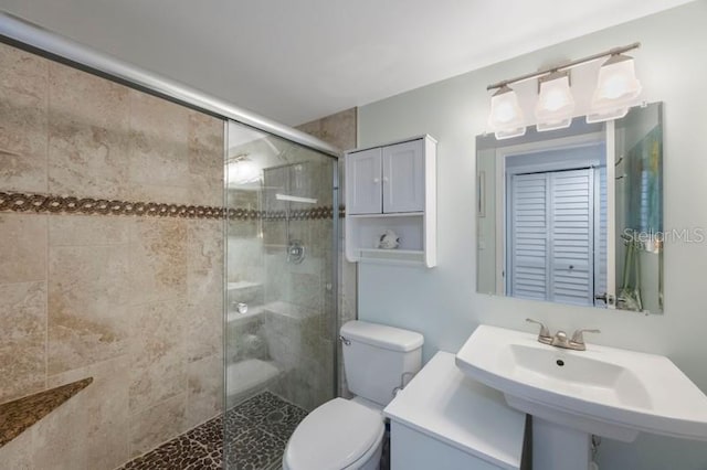 bathroom featuring a shower with shower door, sink, and toilet