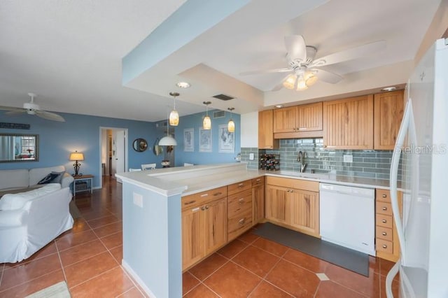 kitchen with a sink, open floor plan, a peninsula, white appliances, and dark tile patterned flooring