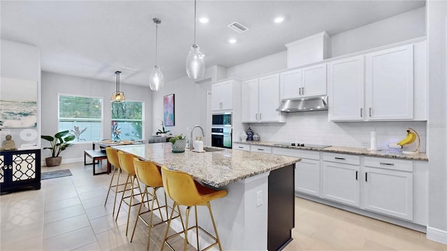 kitchen with pendant lighting, tasteful backsplash, a center island with sink, and white cabinets