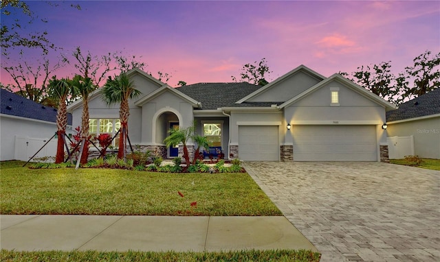view of front facade featuring a garage, a front lawn, stone siding, decorative driveway, and stucco siding