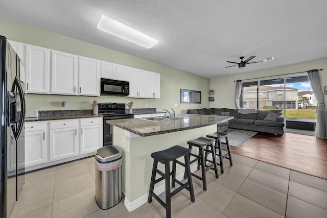 kitchen featuring light tile patterned flooring, white cabinets, a kitchen bar, and black appliances