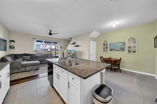 kitchen featuring light tile patterned flooring, white cabinetry, sink, dark stone countertops, and a center island with sink