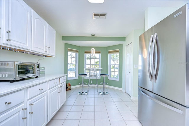 kitchen with stainless steel fridge, white cabinetry, light stone counters, light tile patterned flooring, and decorative light fixtures