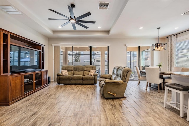 living room with a raised ceiling and ceiling fan with notable chandelier