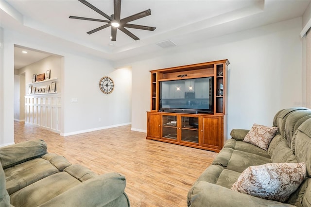 living room with light hardwood / wood-style floors, a raised ceiling, and ceiling fan