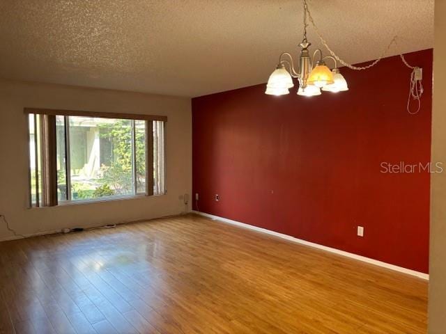 unfurnished room with a textured ceiling, an inviting chandelier, wood finished floors, and baseboards