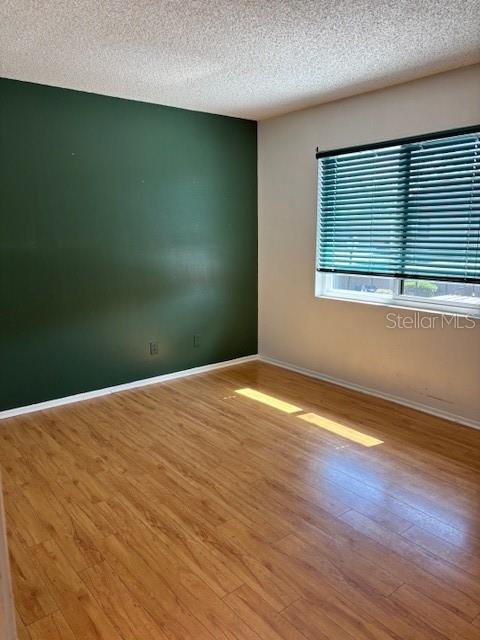 unfurnished room with light wood-style floors, baseboards, and a textured ceiling