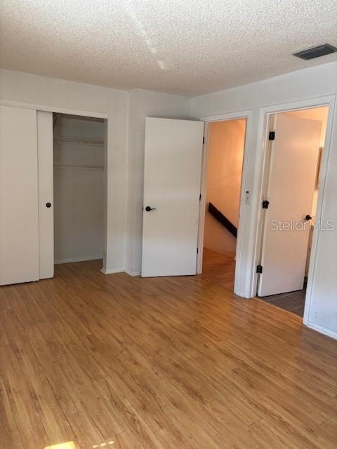 unfurnished bedroom with a textured ceiling, a closet, visible vents, and wood finished floors