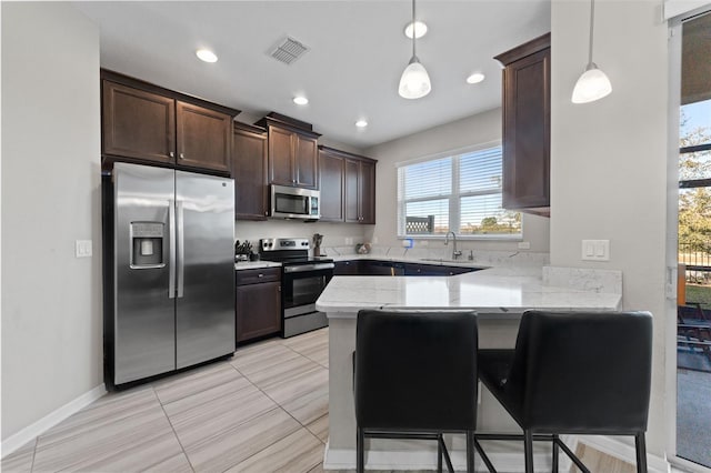 kitchen with light tile patterned flooring, hanging light fixtures, appliances with stainless steel finishes, a kitchen breakfast bar, and kitchen peninsula