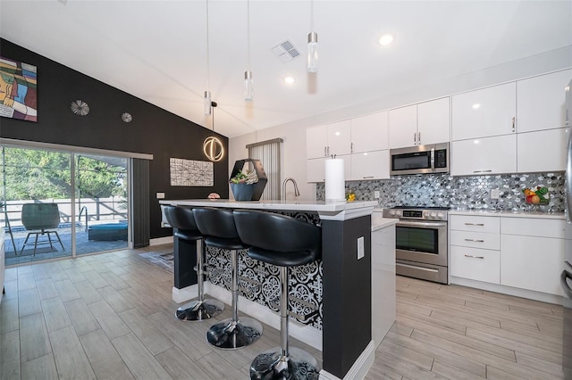 kitchen with vaulted ceiling, appliances with stainless steel finishes, pendant lighting, tasteful backsplash, and a center island with sink