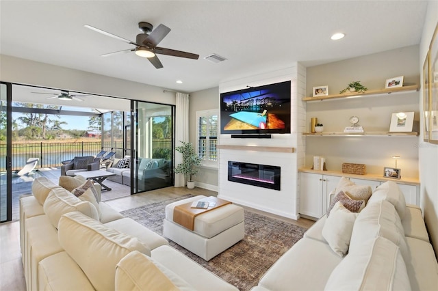 living area with a large fireplace, visible vents, light wood-style flooring, and a healthy amount of sunlight