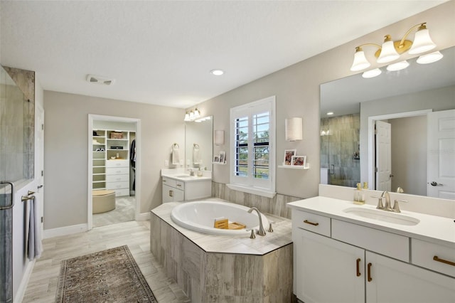 full bath featuring a walk in closet, a stall shower, a garden tub, and a sink