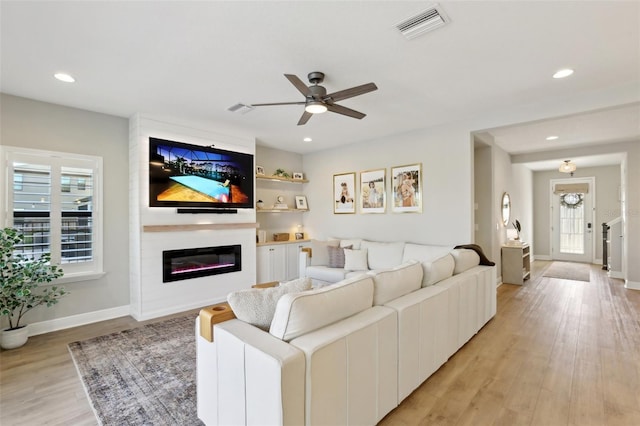 living room with a glass covered fireplace, visible vents, light wood finished floors, and recessed lighting