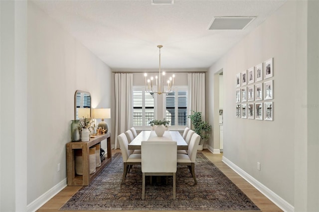 dining room featuring an inviting chandelier, baseboards, visible vents, and wood finished floors