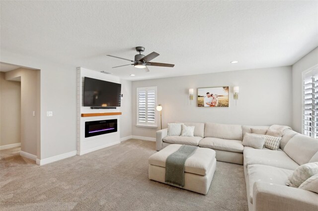 carpeted living area featuring a glass covered fireplace, plenty of natural light, a textured ceiling, and baseboards