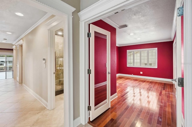 hallway featuring crown molding, light hardwood / wood-style flooring, a textured ceiling, and a wealth of natural light