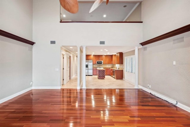 unfurnished living room featuring a high ceiling, ornate columns, and light hardwood / wood-style floors