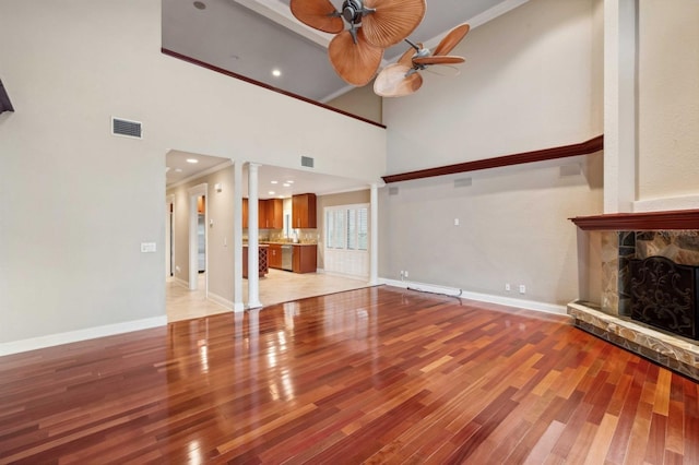 unfurnished living room with ceiling fan, a stone fireplace, light hardwood / wood-style floors, and a towering ceiling