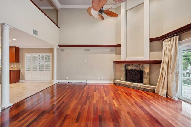 unfurnished living room with decorative columns, ceiling fan, and a stone fireplace