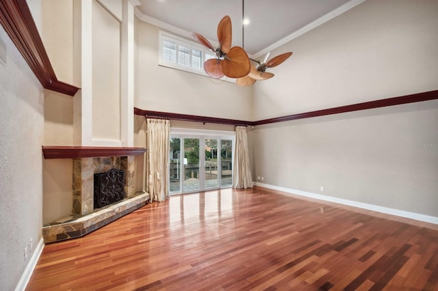 unfurnished living room featuring a towering ceiling, a fireplace, hardwood / wood-style flooring, ornamental molding, and ceiling fan