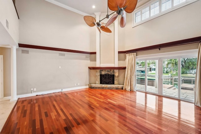 unfurnished living room featuring decorative columns, a high ceiling, ceiling fan, and light hardwood / wood-style floors