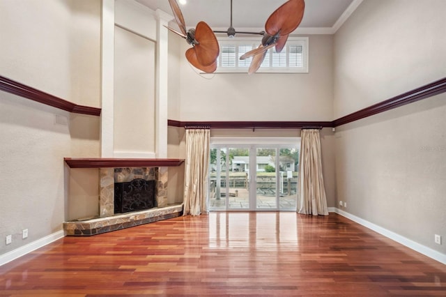 unfurnished living room featuring wood-type flooring, a fireplace, ceiling fan, and crown molding