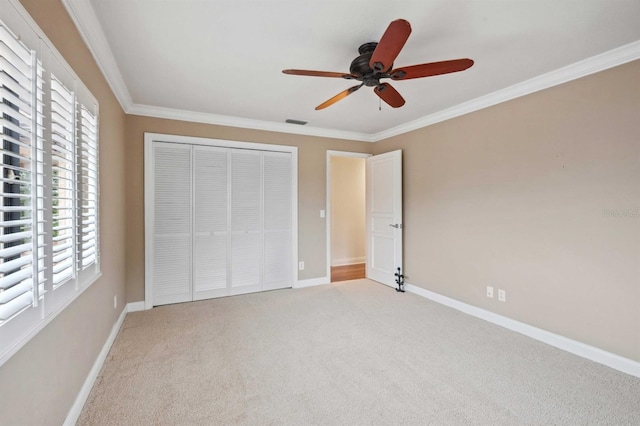 unfurnished bedroom with ceiling fan, a closet, crown molding, and carpet floors