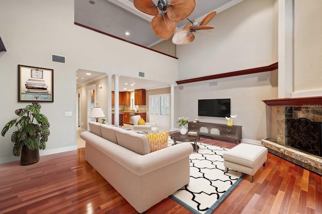 living room featuring a fireplace, ceiling fan, hardwood / wood-style flooring, decorative columns, and crown molding