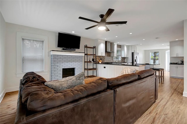 living area with light wood-style flooring, a brick fireplace, baseboards, and ceiling fan