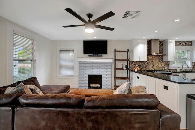 living area with ceiling fan, a wealth of natural light, visible vents, and a fireplace
