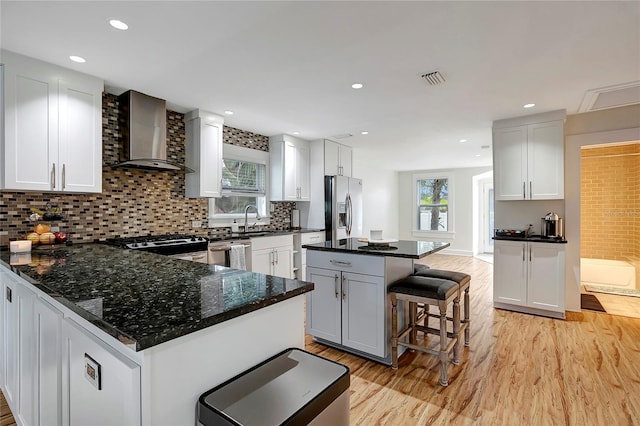 kitchen featuring stainless steel appliances, tasteful backsplash, light wood-type flooring, wall chimney range hood, and a breakfast bar area