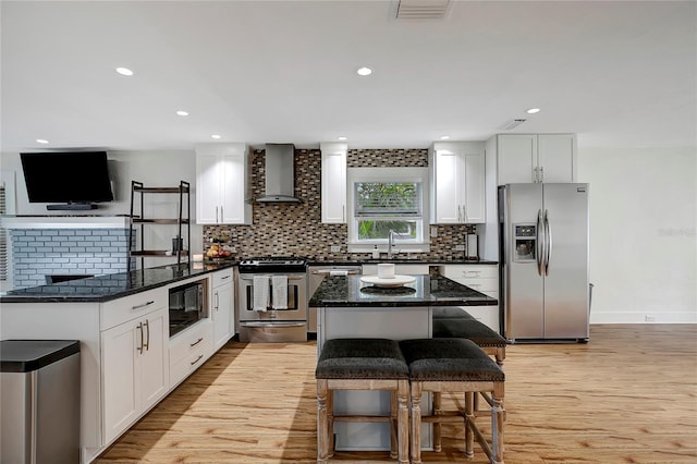 kitchen with white cabinets, light wood-style floors, wall chimney exhaust hood, tasteful backsplash, and appliances with stainless steel finishes