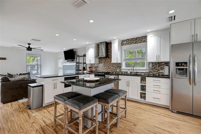 kitchen with stainless steel appliances, a peninsula, open floor plan, visible vents, and wall chimney range hood