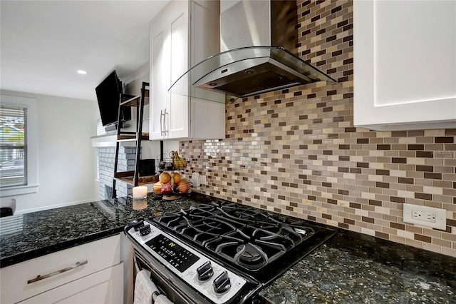 kitchen with wall chimney range hood, stainless steel gas range, decorative backsplash, and white cabinets